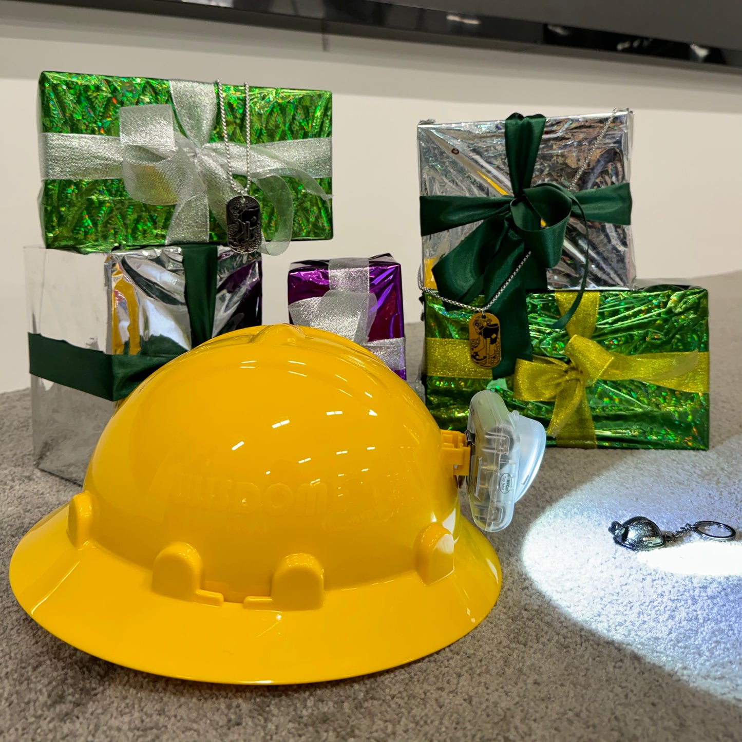 Yellow hard hat on a reflective surface with decorative gift boxes in the background.